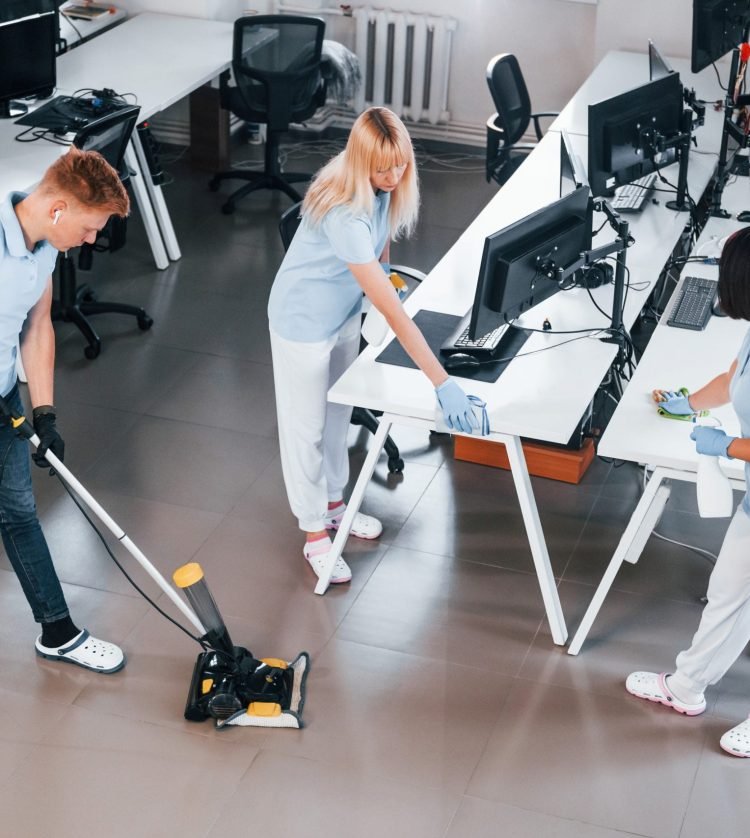 Cleans floor. Group of workers clean modern office together at daytime.