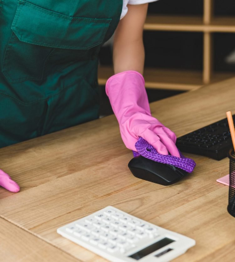 cropped shot of woman in rubber gloves cleaning office table