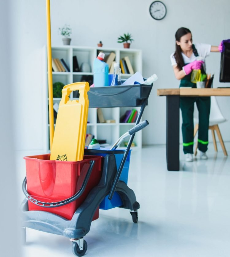 young female janitor cleaning office with various cleaning equipment
